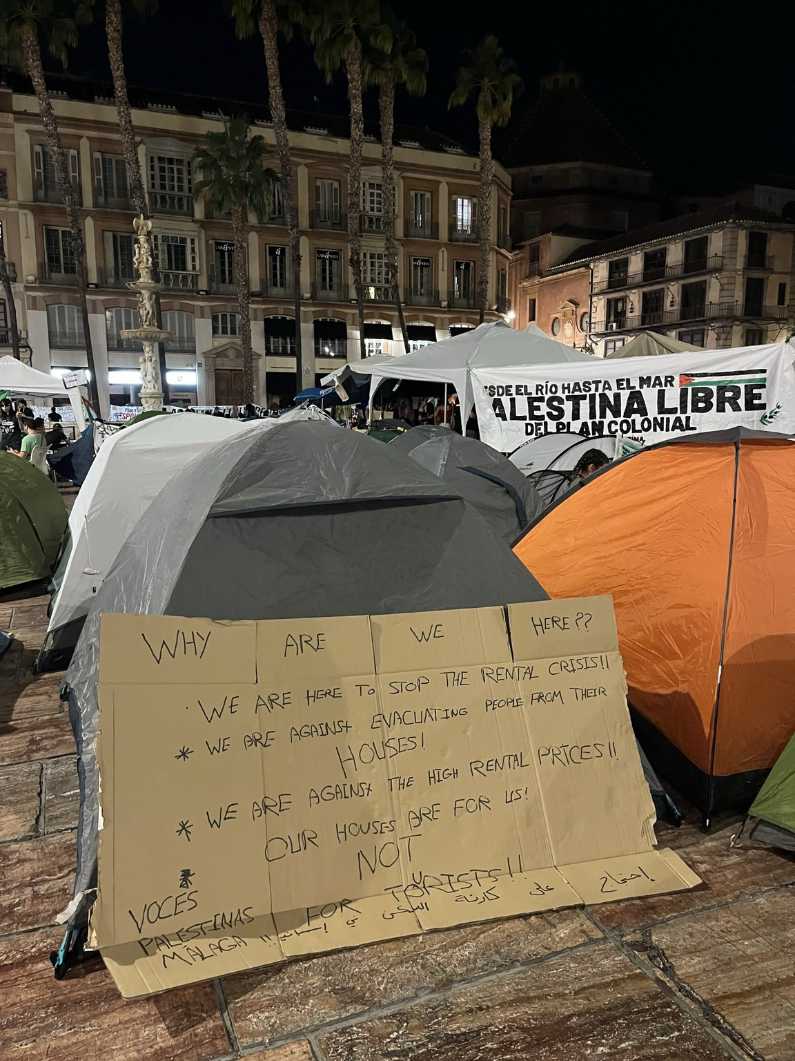 Tienda de campaña con una gran pancarta apoyada realizada por Voces palestinas en la que se lee: WHY ARE WE HERE?? WE ARE HERE TO STOP THE RENTAL CRISIS!! WE ARE AGAINST EVACUATING PEOPLE FROM THEIR HOUSES! WE ARE AGAINST THE HIGH RENTAL PRICES! OUR HOUSES ARE FOR US NOT FOR TOURISTS. Alrededor, muchas otras tiendas de campañas y carpas