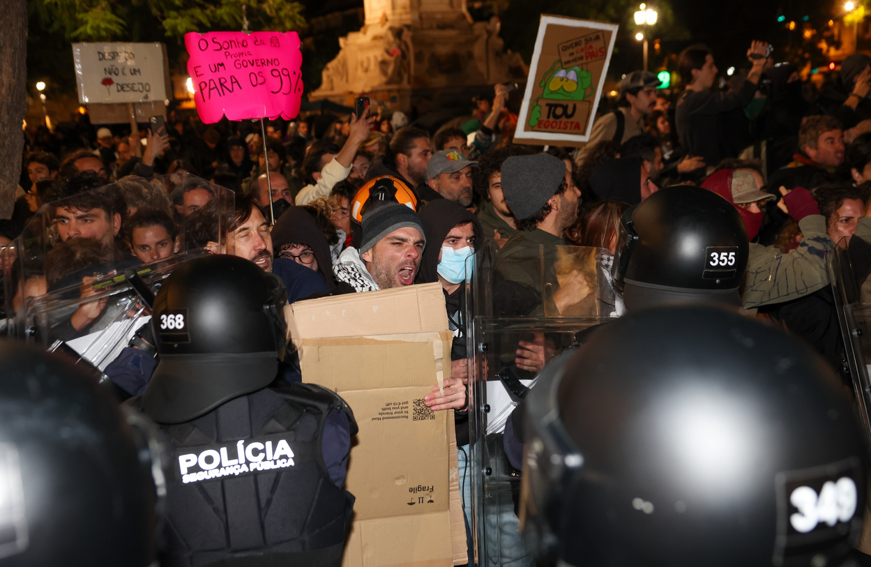 A protestor holding a piece of cardboard in front of riot police.